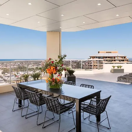 Meriton Suites Bondi Junction Sydney Exterior photo The photo shows a stylish outdoor terrace or balcony area, featuring a long dining table surrounded by several black wire chairs. The table has a centerpiece of vibrant flowers. The space is well-lit, with a clear view of the horizon in the backgroun