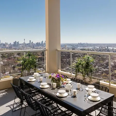 Meriton Suites Bondi Junction Sydney Exterior photo The photo shows a beautifully arranged outdoor dining area on a balcony. There is a long black dining table set for a meal, with plates, glasses, and decorative items like a vase of flowers. Surrounding the table are stylish black chairs. In the back
