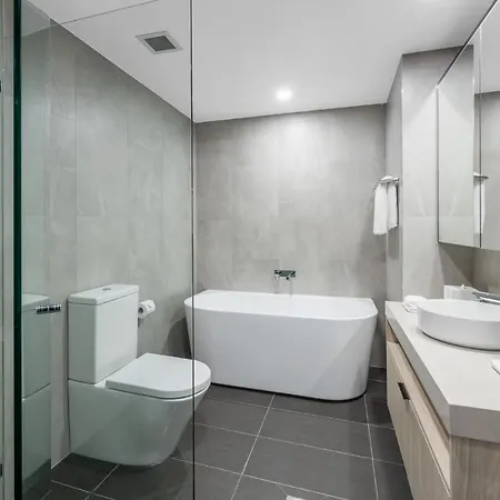 Meriton Suites Bondi Junction Sydney Exterior photo The photo shows a modern bathroom. It features a sleek design with gray tiled walls and dark gray flooring. On the left, there is a toilet and a glass shower enclosure. At the center, a freestanding bathtub is positioned against the wall. To the righ