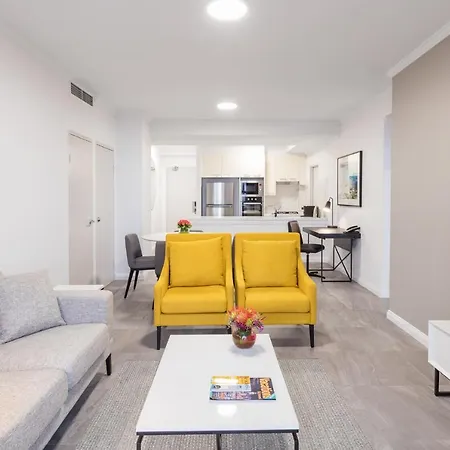 Meriton Suites Bondi Junction Sydney Exterior photo The photo shows a modern living space with a light and airy design. In the foreground, there are two bright yellow armchairs flanking a white coffee table, which has a small vase of flowers and a magazine on it. To the left, there is a light gray sof