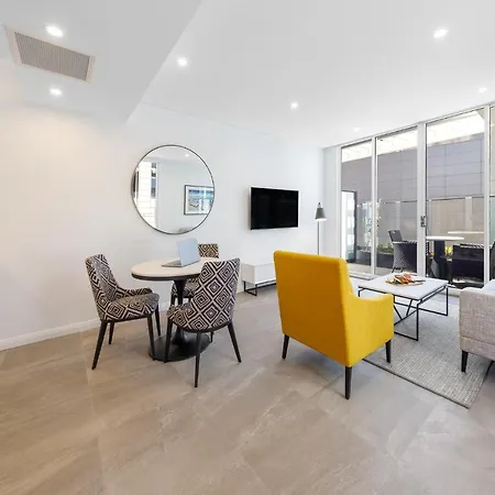 Meriton Suites Bondi Junction Sydney Exterior photo The photo shows a modern and stylish living space. On one side, there is a kitchen area with sleek cabinetry, and next to it, a round dining table surrounded by three patterned chairs. In the center of the room, there is a gray sofa accompanied by a 