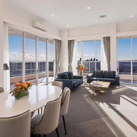 Meriton Suites Bondi Junction Sydney Exterior photo The photo shows a modern and stylish living space with large windows allowing natural light to fill the room. In the foreground, there is a round dining table with several chairs around it, adorned with a floral centerpiece. The seating area features