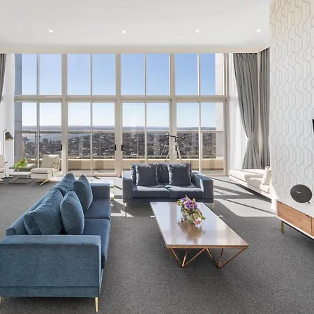 Meriton Suites Bondi Junction Sydney Exterior photo The photo shows a modern and spacious living area. It features large windows that provide a panoramic view of the outside landscape and allow natural light to fill the room. The interior design includes a blue sectional sofa placed in the center, com