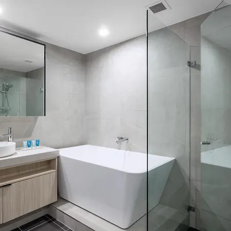 Meriton Suites Bondi Junction Sydney Exterior photo The photo shows a modern bathroom design. It features a spacious bathtub that is white and has a sleek shape. A glass shower enclosure is visible, showcasing a minimalist style. There is a vanity with a round sink and a countertop, accompanied by som