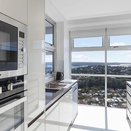 Meriton Suites Bondi Junction Sydney Exterior photo The photo shows a modern kitchen with sleek, shiny white cabinets and a large window that offers a panoramic view of the outside landscape. The kitchen features built-in appliances, including an oven and a stove, with a stylish countertop. The spacio