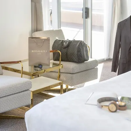 Meriton Suites Bondi Junction Sydney Exterior photo The photo depicts an elegant hotel room or living space. In the foreground, there's a neatly made bed with white linens. To the side, there are two stylish armchairs in a light fabric, accompanied by a side table with a decorative item or small acces