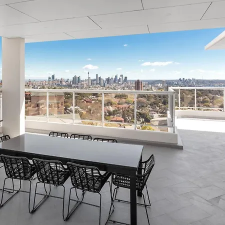 Meriton Suites Bondi Junction Sydney Exterior photo The photo shows a modern outdoor balcony or terrace space with a dining table and chairs. The table is black and has a minimalist design, surrounded by stylish chairs. In the background, there is a stunning view of a city skyline under a clear blue s