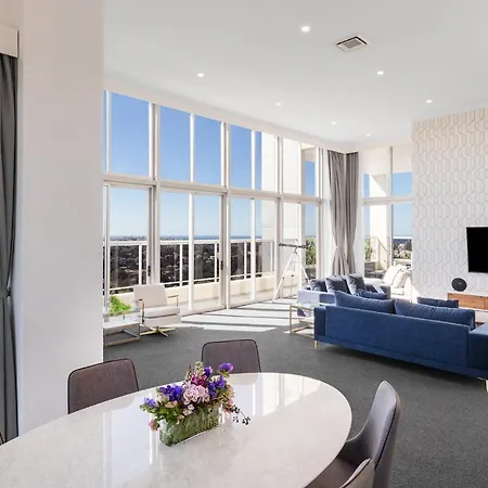 Meriton Suites Bondi Junction Sydney Exterior photo The photo shows a bright and modern living space with large windows that allow plenty of natural light to fill the room. The interior features a stylish and comfortable blue sofa facing a mounted television on the wall. There is a round dining table 