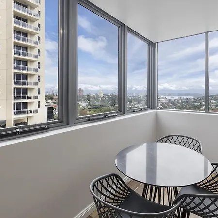 Meriton Suites Bondi Junction Sydney Exterior photo The photo shows a modern interior space with large windows providing a view of the outside. There is a round table at the center surrounded by four black wire chairs, creating a cozy seating area. Through the windows, you can see a cityscape with a t